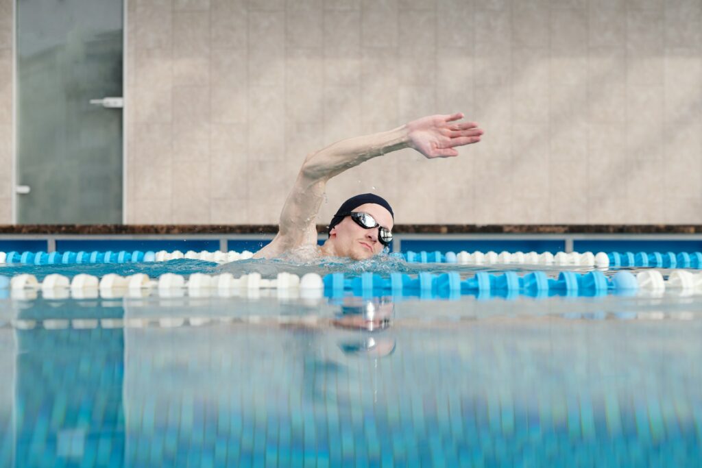 Een zwemmer met duikbril en badmuts op steekt zijn arm omhoog tijdens het zwemmen.