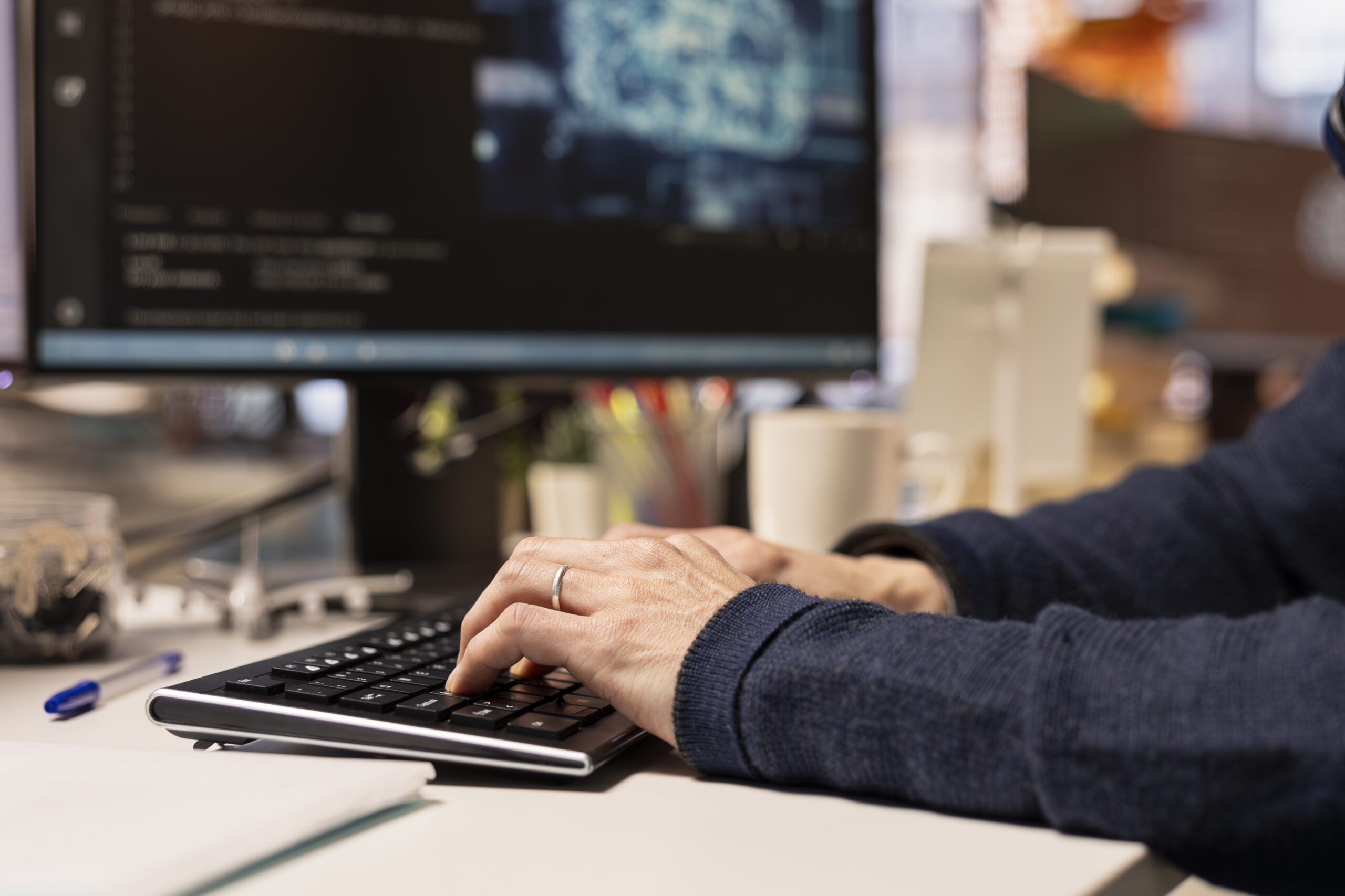 Persoon typt op toetsenbord met computerscherm op de achtergrond.