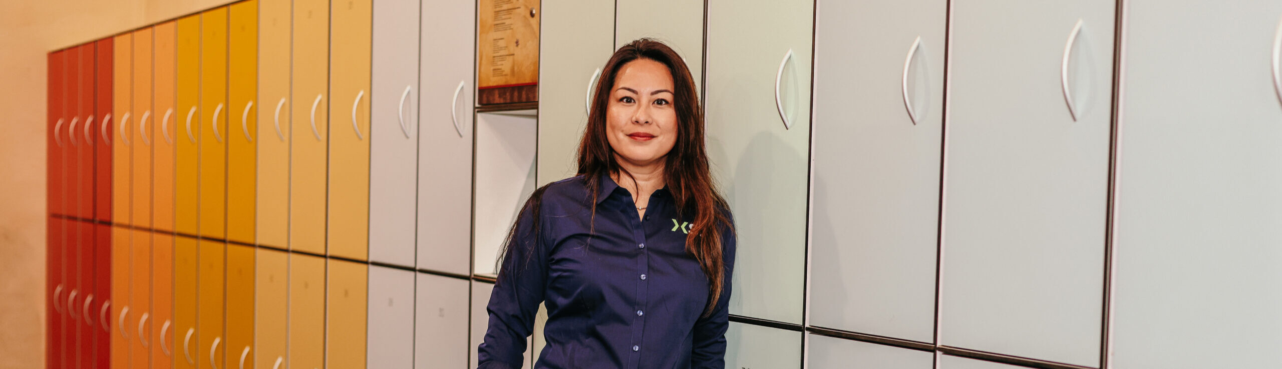Vrouw in XS2-bedrijfskleding staat voor gekleurde lockers. Vrouw in XS2-bedrijfskleding staat voor gekleurde lockers.