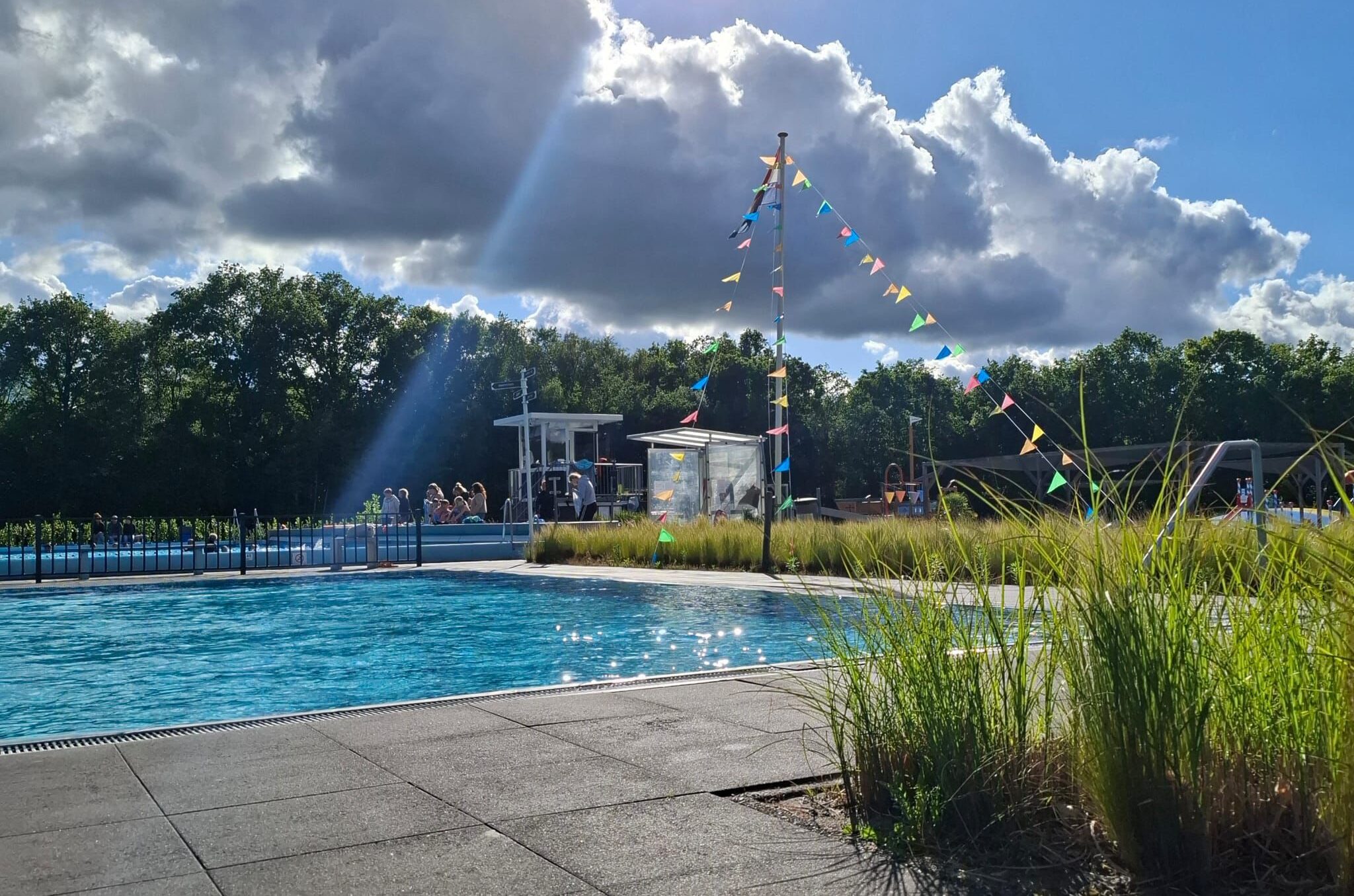 Buitenzwembad met feestelijke vlaggetjes en zonnestralen door de wolken.