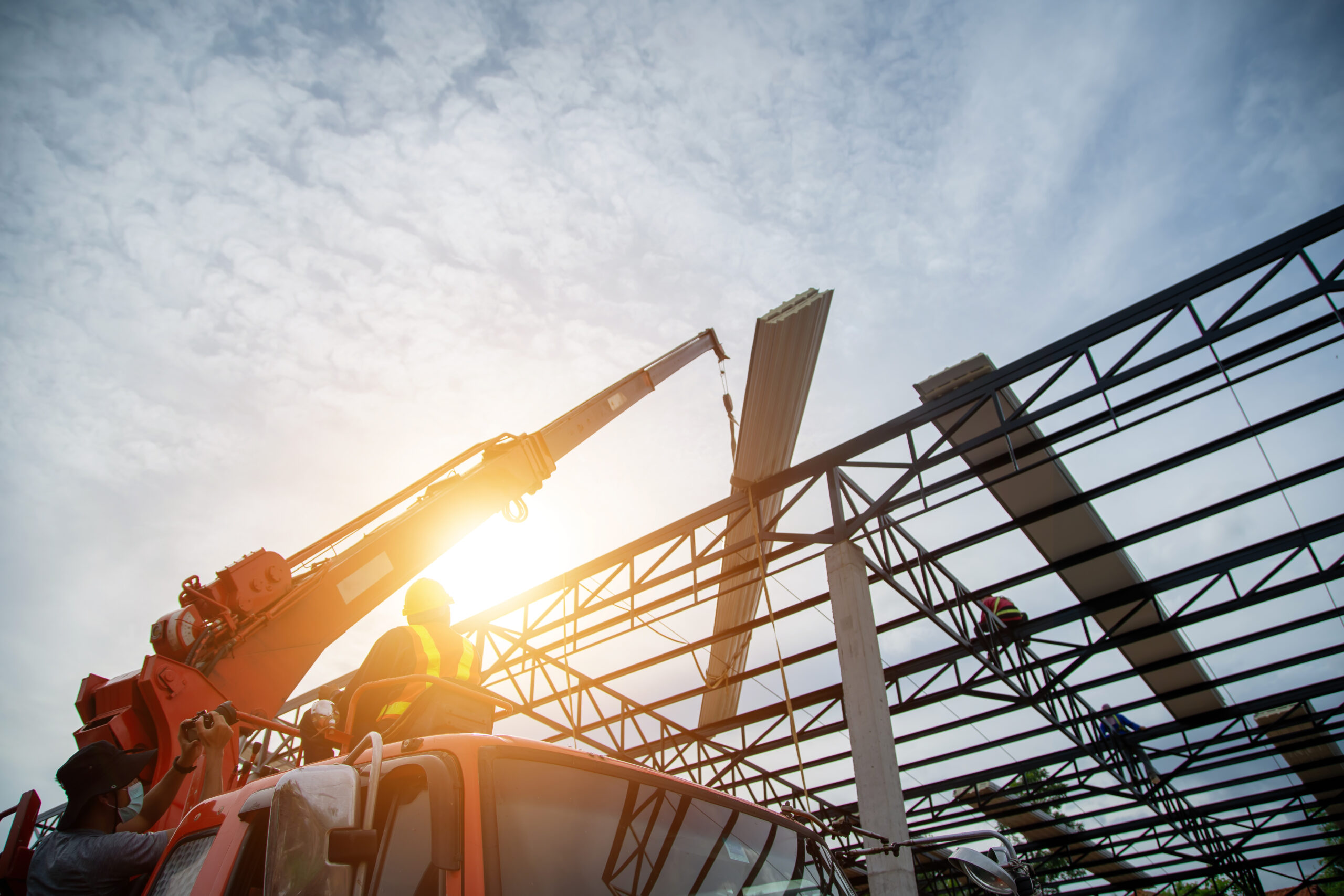 Bouwvakkers plaatsen dakpanelen met behulp van een kraan op een staalconstructie.